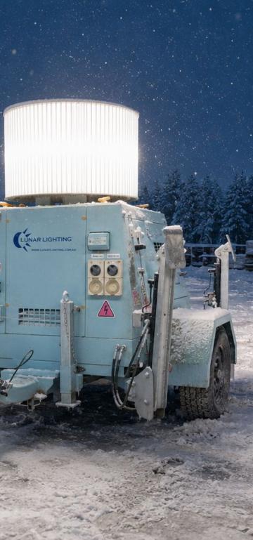 Lunar Lighting light tower lighting a snow-covered work site at dusk